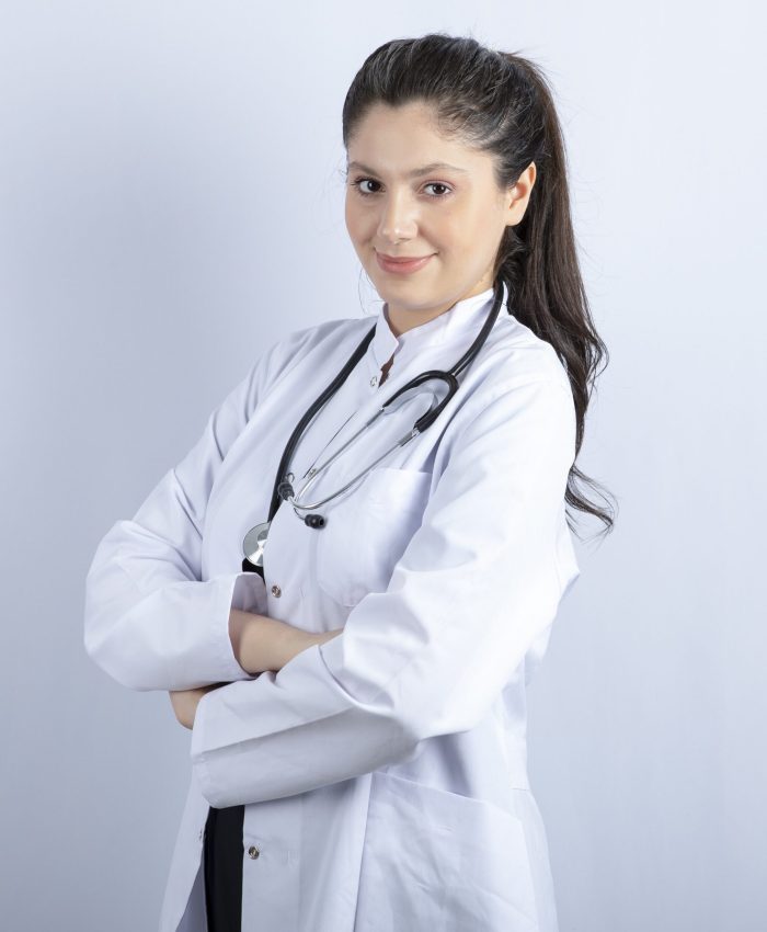 Beautiful female doctor in white coat standing arms crossed over white wall Beautiful female doctor in white coat standing arms crossed over white wall